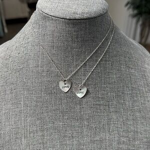Two silver necklaces with a silver heart pendant engraved with the word Love.